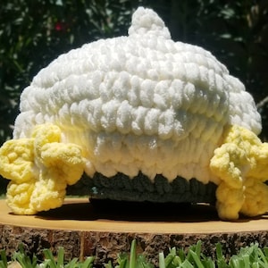 May include: A white crocheted hat with yellow crocheted flowers on the sides. The hat is sitting on a wooden surface.