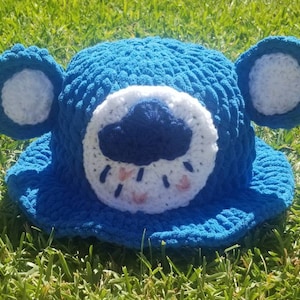 Peut inclure: Chapeau bleu en crochet avec des oreilles blanches et un visage blanc avec un nuage bleu et des gouttes de pluie.