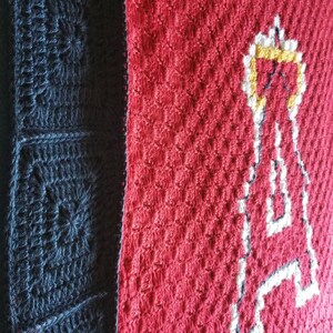 May include: A crocheted blanket with a red and black color scheme. The red side features a white crocheted letter "A" with a yellow outline.