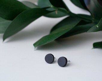 May include: A pair of black leather stud earrings. The earrings are round and have a textured surface.