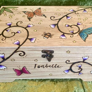 May include: Wooden box with a floral design and butterflies. The box is personalised with the name "Isabelle".