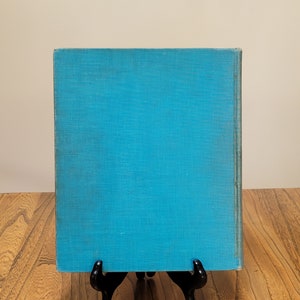 K&ouml;nnte beinhalten: Ein blaues Hardcover-Buch mit einem strukturierten Einband. Das Buch steht auf einer Holzoberfl&auml;che.
