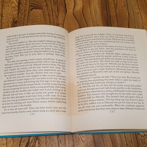 K&ouml;nnte beinhalten: Ein altes Buch, das auf den Seiten 8 und 9 aufgeschlagen ist und eine Schwarzwei&szlig;illustration einer von Pferden gezogenen Kutsche mit Passagieren zeigt. Der Text auf der Seite beschreibt eine Reise in einer Pferdekutsche.