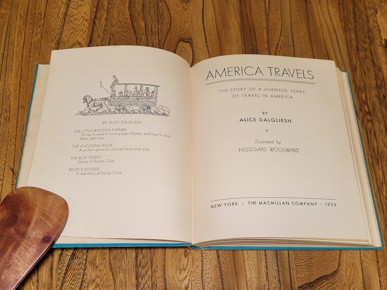 K&ouml;nnte beinhalten: Ein ge&ouml;ffnetes Buch mit einem blauen Einband. Das Buch tr&auml;gt den Titel "America Travels: The Story of a Hundred Years of Travel in America" von Alice Dalgliesh, illustriert von Hildegarde Woodward. Das Buch wurde 1933 von The Macmillan Company ver&ouml;ffentlicht.