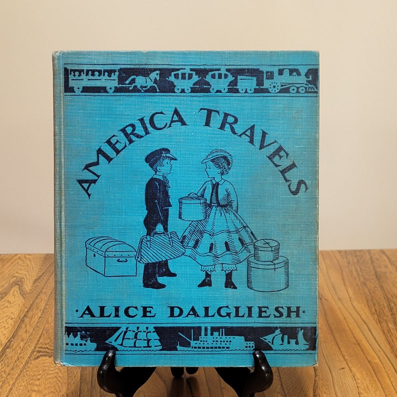 K&ouml;nnte beinhalten: Ein blauer Buchumschlag mit dem Titel "America Travels" in wei&szlig;en Buchstaben. Das Buch zeigt Illustrationen von zwei Kindern mit Koffern und einem Zug, und der Name des Autors, "Alice Dalgliesh", ist unter dem Titel gedruckt.