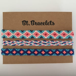 Puede incluir: Tres pulseras de la amistad con un patrón geométrico en tonos de azul, rosa y blanco. Las pulseras se muestran en una tarjeta marrón con el texto "Bt. Bracelets".