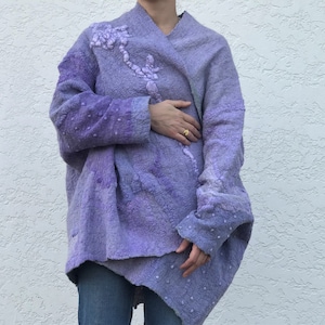 May include: A long, purple, felted cardigan with a floral design on the front. The cardigan is open in the front and has a relaxed fit.