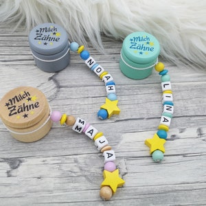 Könnte beinhalten: Zwei Holzkisten mit dem Text "Milch Zähne" und einem Sternendesign. Jede Kiste ist an einer Holzperlenkette mit den Namen "Maja", "Noah" und "Lina" befestigt, die in weißen Buchstaben auf blauen, rosa und türkisfarbenen Perlen geschrieben sind.