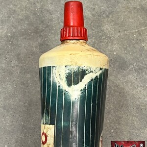 Puede incluir: Botella vintage con tapa roja y cuerpo cil&iacute;ndrico. El cuerpo es principalmente blanco con un patr&oacute;n de rayas verdes y blancas. Una peque&ntilde;a etiqueta descolorida es visible cerca de la base. La botella muestra signos de edad y desgaste.