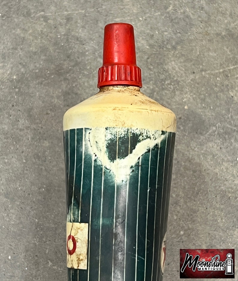 Puede incluir: Botella vintage con tapa roja y cuerpo cil&iacute;ndrico. El cuerpo es principalmente blanco con un patr&oacute;n de rayas verdes y blancas. Una peque&ntilde;a etiqueta descolorida es visible cerca de la base. La botella muestra signos de edad y desgaste.