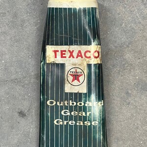 Puede incluir: Tubo de grasa para engranajes fueraborda Texaco vintage. El tubo tiene una tapa roja y una parte superior blanca. El cuerpo es de color verde oscuro con rayas verticales y el logotipo de Texaco. El texto "Outboard Gear Grease" est&aacute; impreso.
