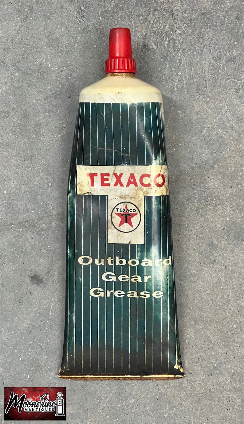 Puede incluir: Tubo de grasa para engranajes fueraborda Texaco vintage. El tubo tiene una tapa roja y una parte superior blanca. El cuerpo es de color verde oscuro con rayas verticales y el logotipo de Texaco. El texto "Outboard Gear Grease" est&aacute; impreso.