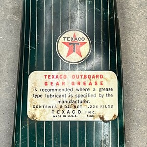 Puede incluir: Lata de grasa para engranajes fueraborda Texaco vintage. La lata es de color verde oscuro con rayas verticales blancas. El logotipo de Texaco es una estrella roja dentro de un c&iacute;rculo blanco. La etiqueta dice "TEXACO OUTBOARD GEAR GREASE" y "CONTENIDO 226 gramos".