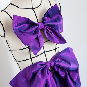 Peut inclure: Un mannequin portant deux grands n&oelig;uds violets iris&eacute;s, un sur la poitrine et un &agrave; la taille.