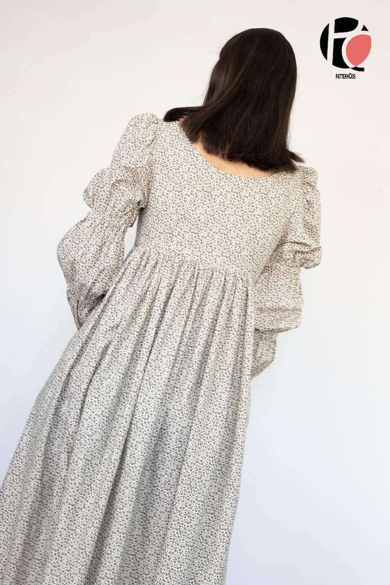 May include: A long, light-colored dress with a floral pattern. The dress features long sleeves with puffed shoulders and a gathered skirt. The model is seen from the back, with the dress's details clearly visible against a white background.