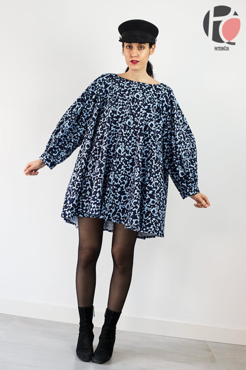 May include: A blue and black leopard print mini dress with long sleeves and a round neckline. The dress is worn with black tights and black ankle boots. The model is wearing a black newsboy cap.