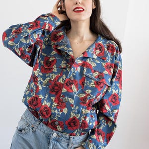 Pu&ograve; includere: Una giacca di jeans blu con un motivo floreale rosso e bianco. La giacca ha un colletto, maniche lunghe e una chiusura con bottoni.