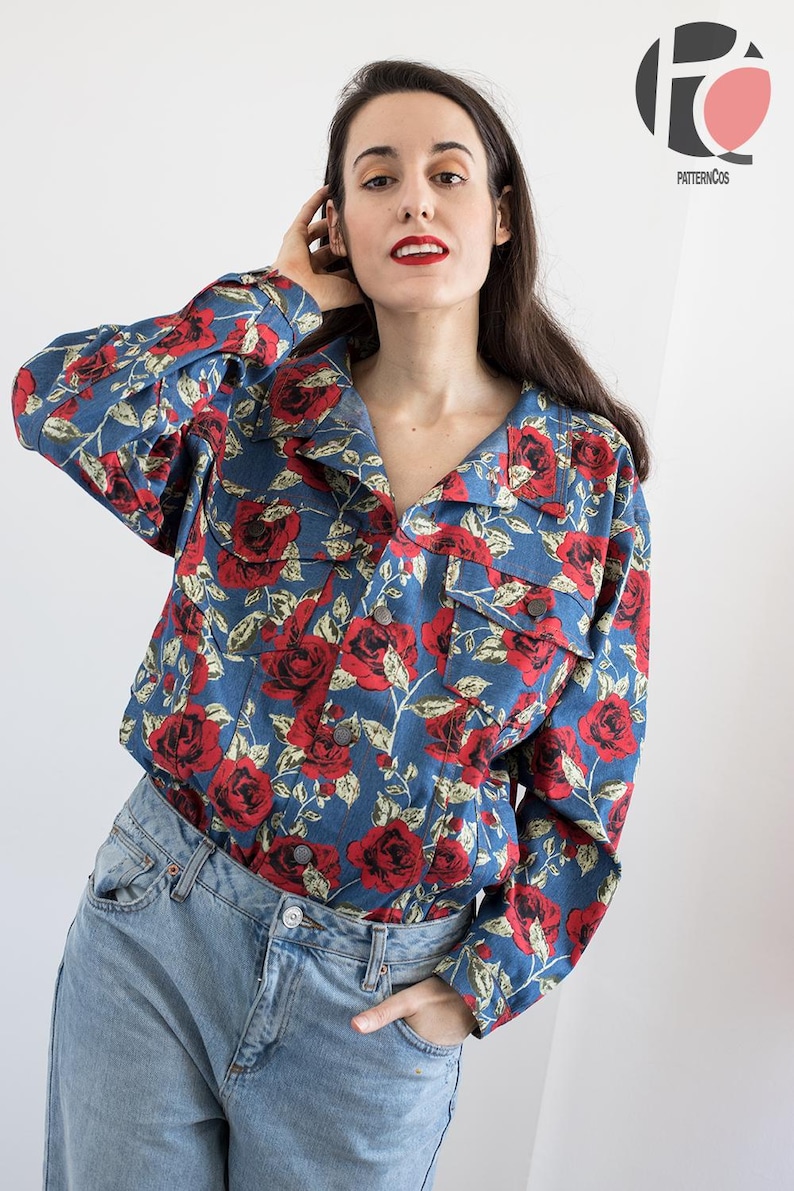 Pu&ograve; includere: Una giacca di jeans blu con un motivo floreale rosso e bianco. La giacca ha un colletto, maniche lunghe e una chiusura con bottoni.