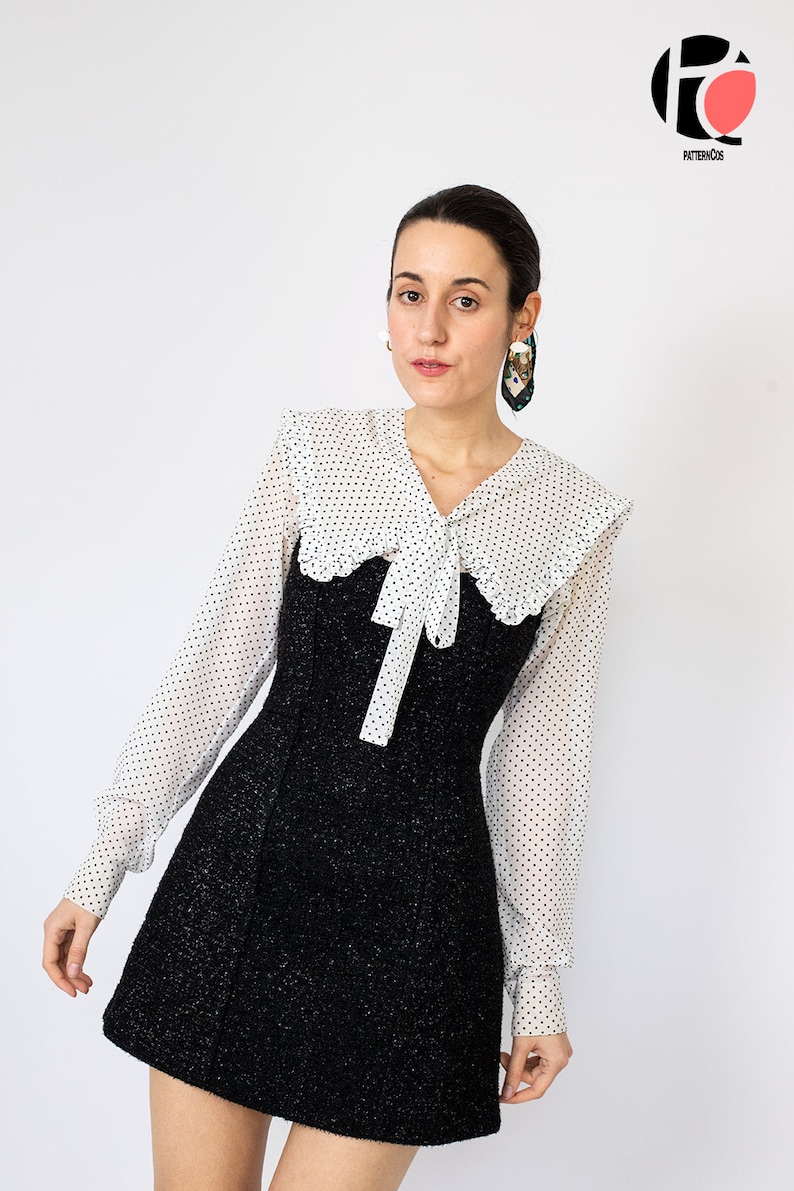 K&ouml;nnte beinhalten: Ein schwarzes Tweed-Minikleid mit einer wei&szlig;en Bluse mit Polka Dots, die einen gro&szlig;en Kragen und eine Schleife aufweist. Das Kleid hat lange &Auml;rmel und ein figurbetontes Oberteil. Das Model tr&auml;gt gro&szlig;e Ohrringe und hat dunkles Haar.