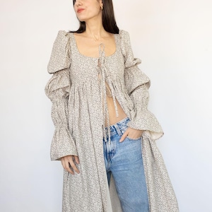 May include: A long, beige floral print dress with a square neckline and long, ruffled sleeves. The dress is open in the front and worn with blue jeans. The PatternCos logo is in the upper right corner.