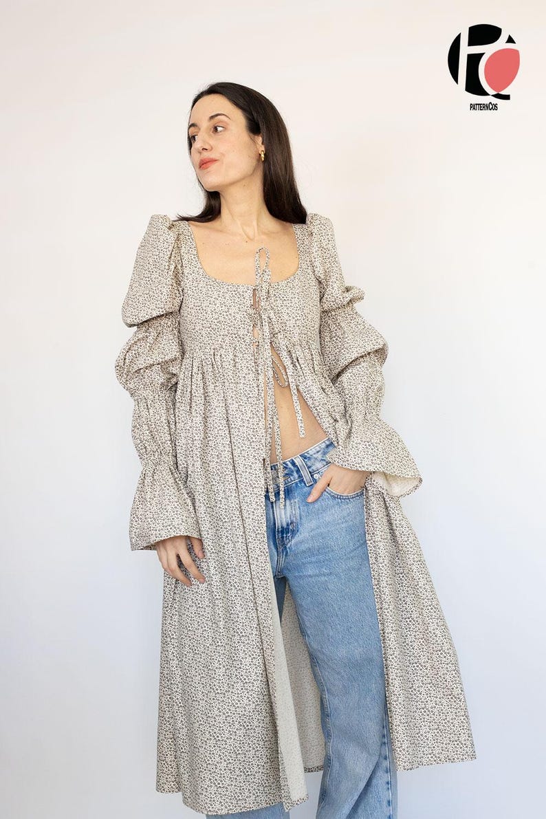 May include: A long, beige floral print dress with a square neckline and long, ruffled sleeves. The dress is open in the front and worn with blue jeans. The PatternCos logo is in the upper right corner.