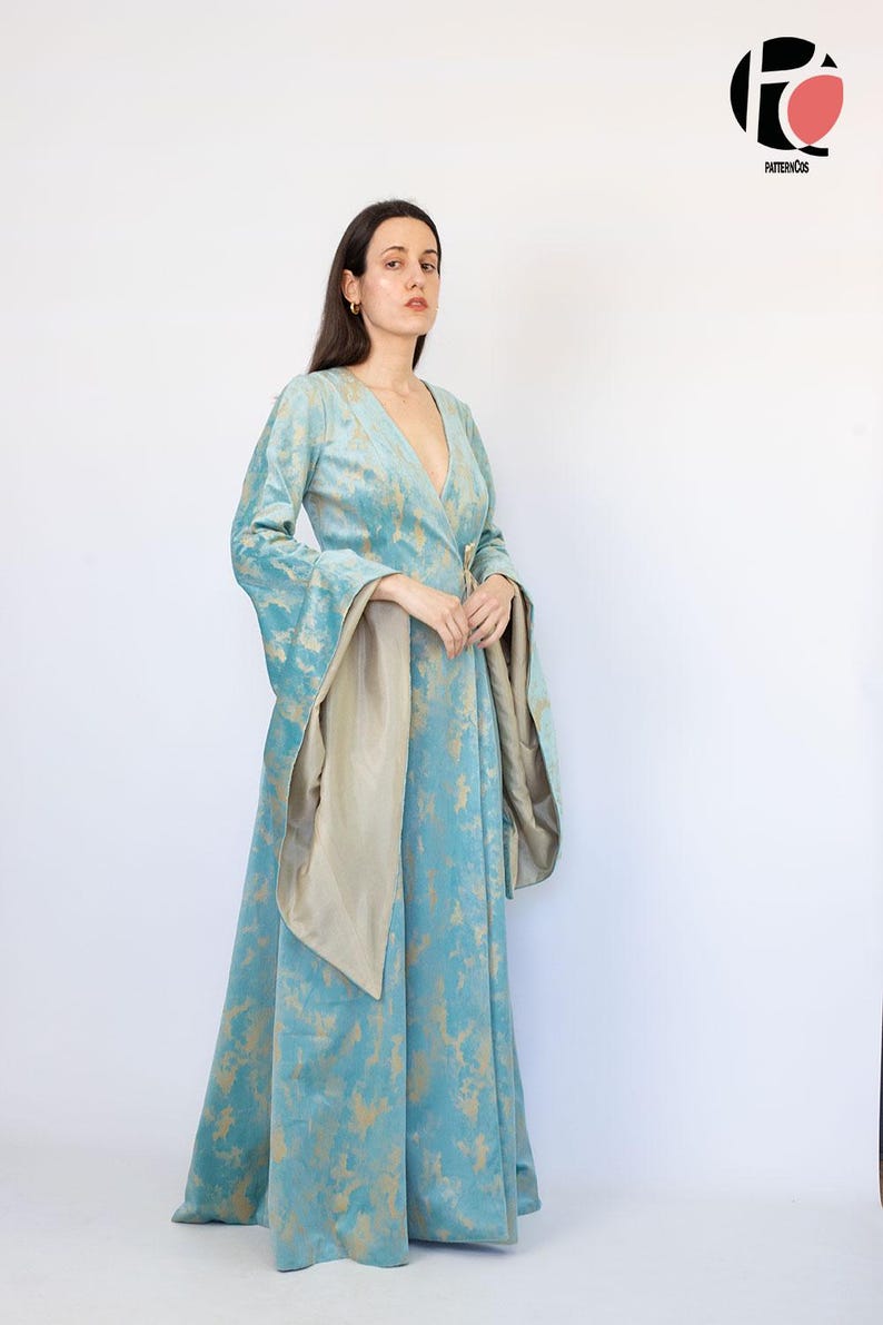 May include: A long, flowing teal dress with gold accents and wide sleeves. The dress features a wrap-style front and a matching sash. The fabric has a soft, velvety texture. The dress is suitable for special occasions.