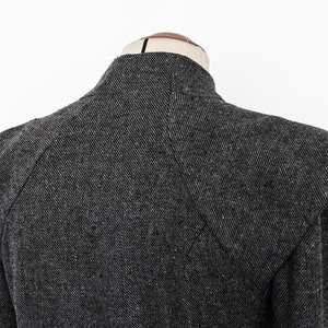 May include: A black and gray tweed jacket with a high collar and large shoulder pads.