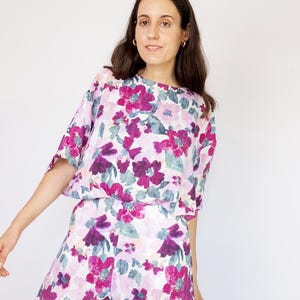 May include: A woman wearing a white and purple floral print top and matching shorts. The top has a relaxed fit and short sleeves. The shorts are high-waisted and have a wide leg.