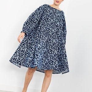May include: A woman wearing a blue and white animal print dress with a loose fit and long sleeves. She is wearing beige heeled sandals.