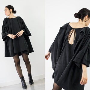 May include: A black, loose-fitting dress with a low back and a tie detail. The dress has long, wide sleeves with a layered ruffle detail.