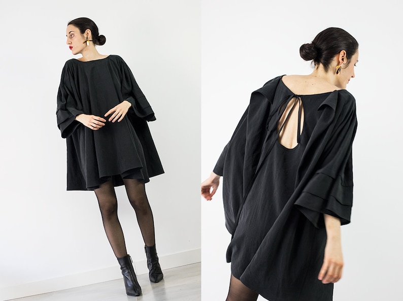 May include: A black, loose-fitting dress with a low back and a tie detail. The dress has long, wide sleeves with a layered ruffle detail.