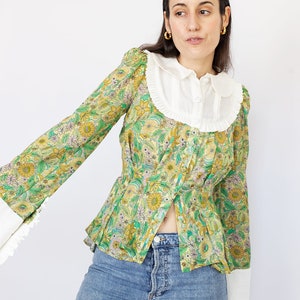 May include: A green and yellow floral print blouse with a white Peter Pan collar and long sleeves. The blouse has a fitted waist and a slightly flared hem.