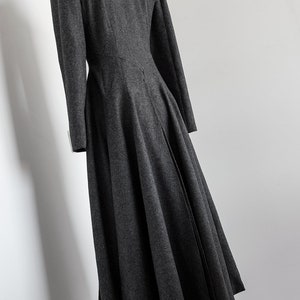 May include: A long, dark gray wool coat with a high collar and a fitted bodice. The coat has a flared skirt and a back vent.