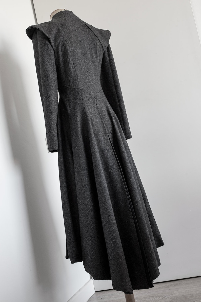 May include: A long, dark gray wool coat with a high collar and a fitted bodice. The coat has a flared skirt and a back vent.