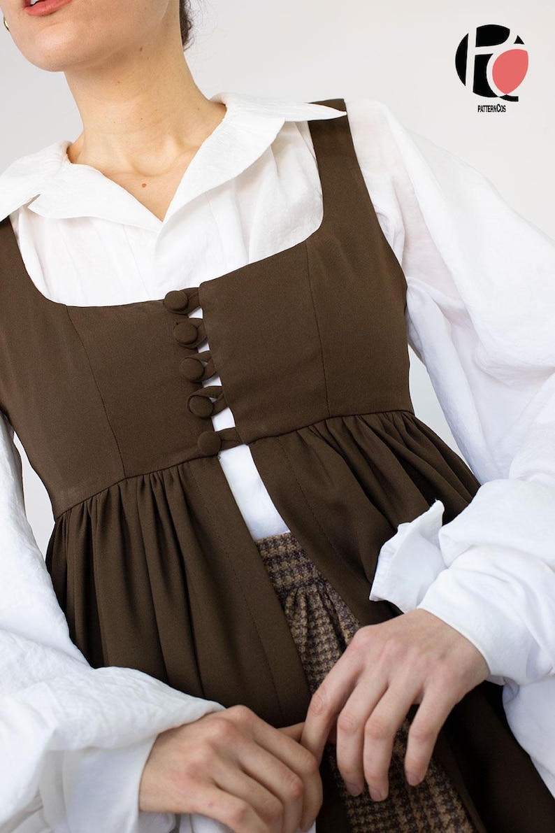 May include: A brown sleeveless dress with a square neckline and button details, layered over a white collared shirt. The dress has a gathered skirt and is paired with a patterned skirt. The image features the logo "PATTERNCOS".