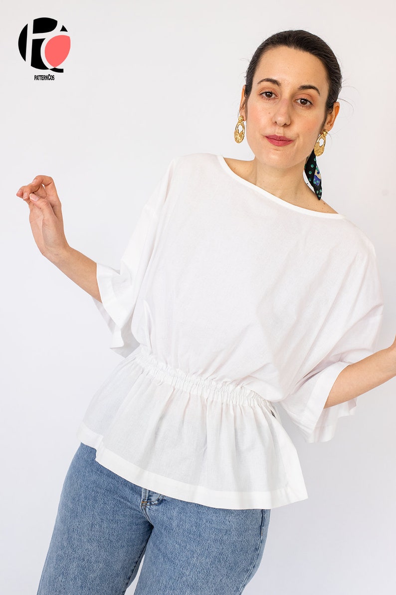 May include: A white, loose-fitting blouse with a gathered elastic waistband and 3/4 sleeves. The blouse is made of a lightweight fabric and has a relaxed fit.