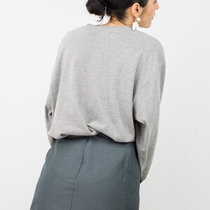 May include: A woman wearing a gray long-sleeved shirt and a dark green mini skirt.