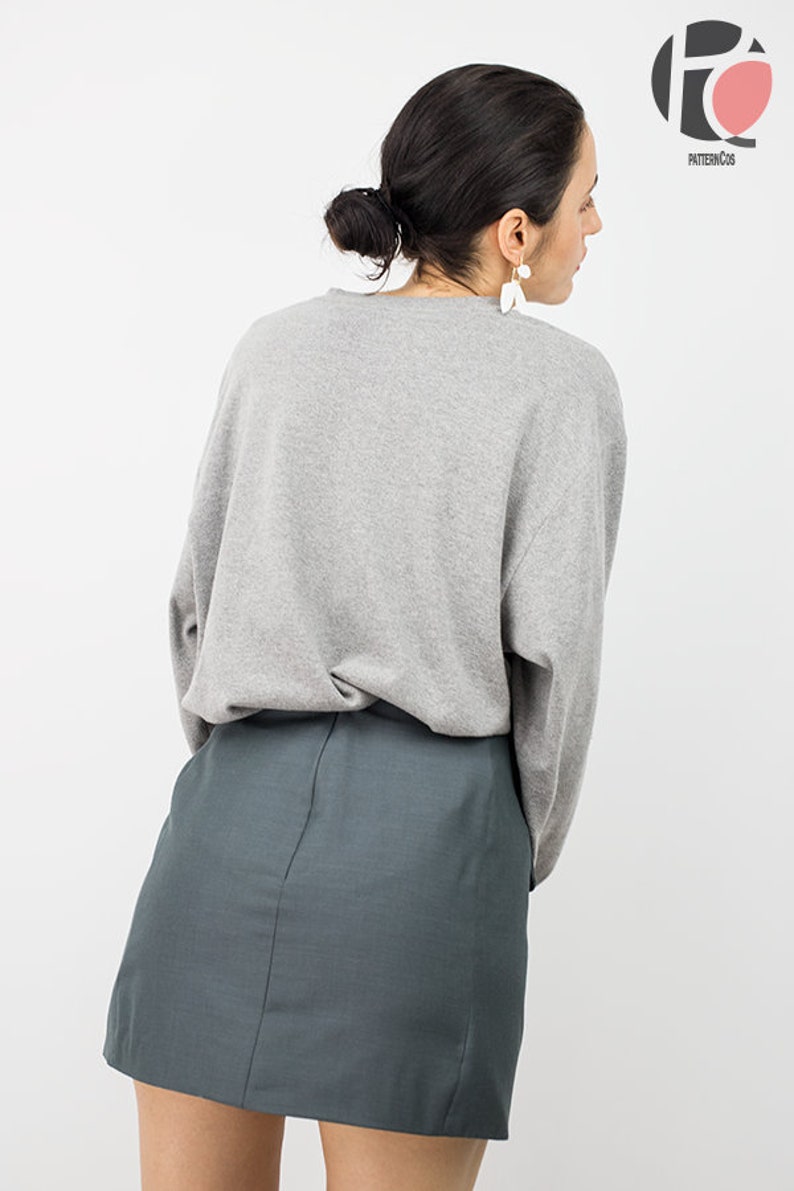 May include: A woman wearing a gray long-sleeved shirt and a dark green mini skirt.