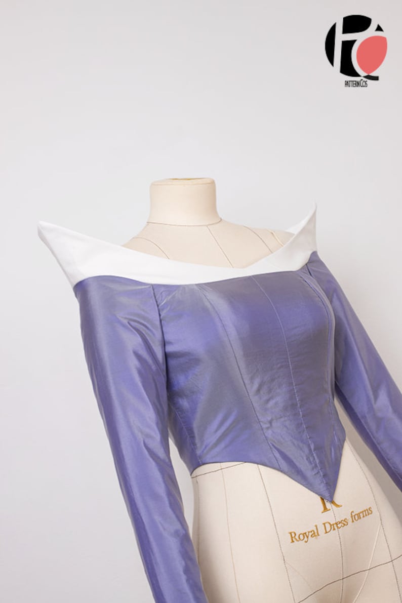Peut inclure: Un corsage violet avec un col blanc et des manches longues. Le corsage est ajust&eacute; et a une taille pointue. Le tissu est brillant et a un l&eacute;ger &eacute;clat. Le corsage est sur un mannequin.
