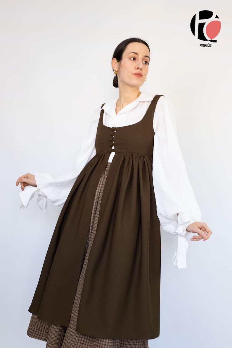 May include: A brown pinafore dress with a square neckline and button details, layered over a white blouse with voluminous sleeves. The dress is paired with a patterned skirt. The logo "PATTERNCOS" is in the top right corner.