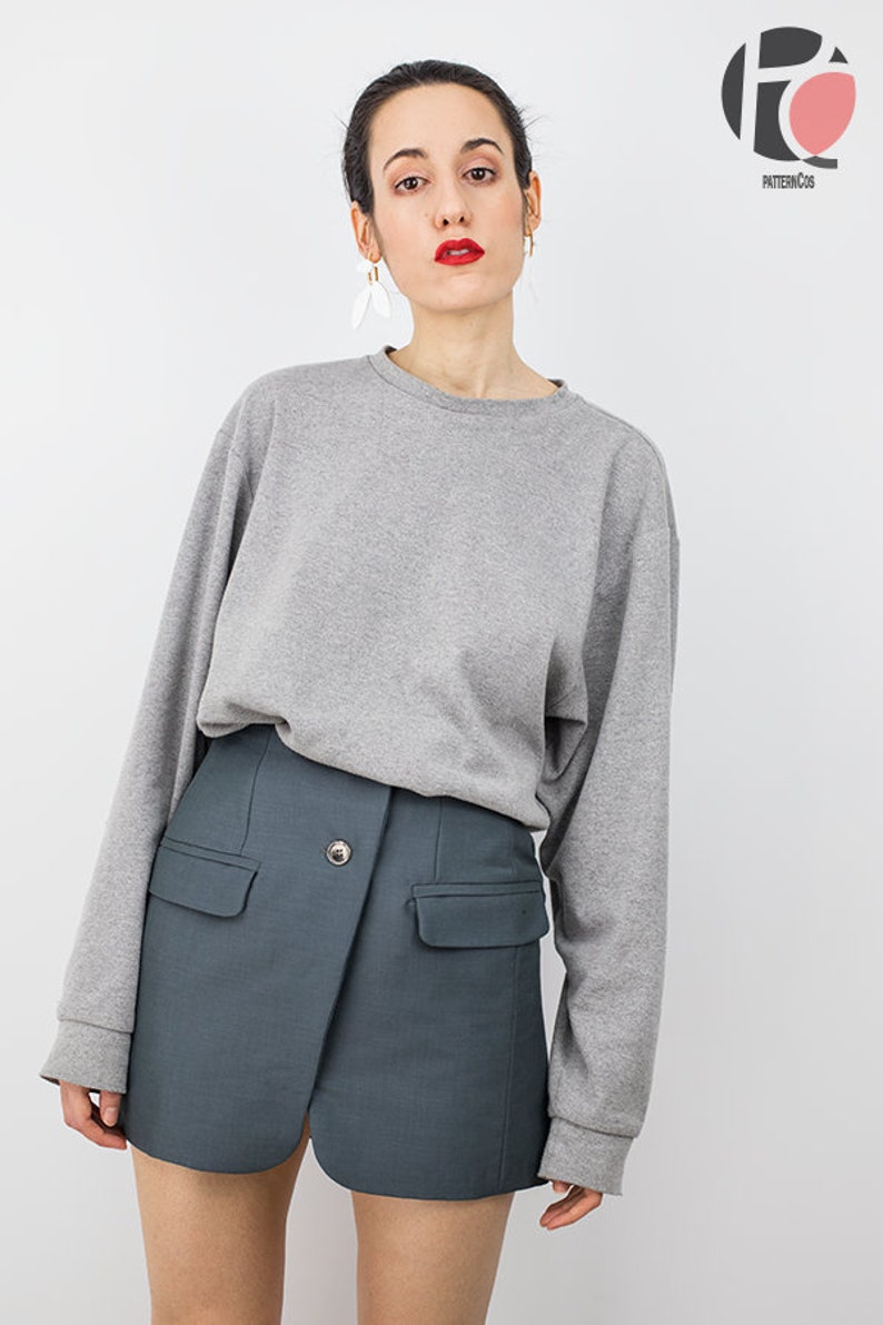 May include: A woman wearing a gray long-sleeved sweatshirt and a dark blue mini skirt with a single button closure and two pockets.