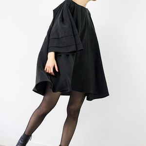May include: A black mini dress with a wide, flowing skirt and long, bell-shaped sleeves. The dress is worn with black tights and black ankle boots.