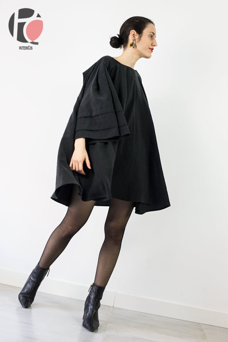 May include: A black mini dress with a wide, flowing skirt and long, bell-shaped sleeves. The dress is worn with black tights and black ankle boots.