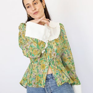 May include: A green and yellow floral print blouse with a white Peter Pan collar and white cuffs. The blouse has a fitted bodice and a slightly flared hem.