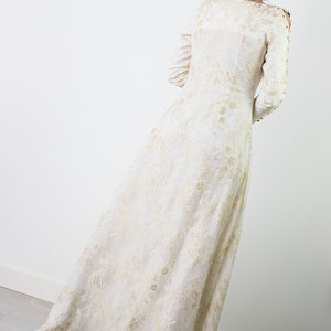 Peut inclure: Une robe maxi blanche avec des broderies dor&eacute;es. La robe a des manches longues et un col rond. La robe est faite d'un tissu transparent et a une silhouette fluide.