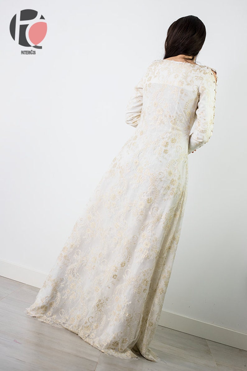 Peut inclure: Une robe maxi blanche avec des broderies dor&eacute;es. La robe a des manches longues et un col rond. La robe est faite d'un tissu transparent et a une silhouette fluide.