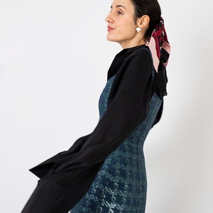 K&ouml;nnte beinhalten: Eine Frau tr&auml;gt ein schwarzes Langarm-Oberteil &uuml;ber einem blau-gr&uuml;nen Mini-Kleid mit Hahnentrittmuster. Ein gemustertes Halstuch und wei&szlig;e Ohrringe vervollst&auml;ndigen den Look. Das Bild ist vor einem wei&szlig;en Hintergrund aufgenommen.
