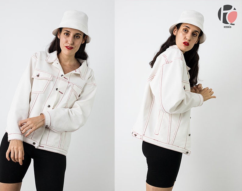 Pu&ograve; includere: Una giacca di jeans bianca con cuciture rosse. La giacca ha una chiusura con bottoni e due tasche sul davanti. La modella indossa pantaloncini neri e un cappello a secchiello bianco.