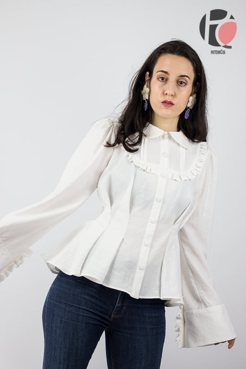 May include: A white button-up blouse with a ruffled collar and cuffs. The blouse has a fitted bodice and a flared skirt. The model is wearing blue jeans.