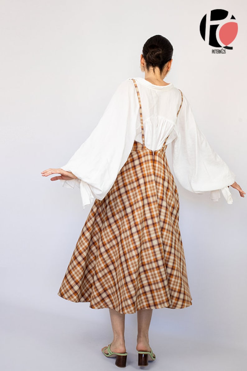 Pode incluir: Uma saia xadrez marrom e bege com uma blusa branca e um par de sand&aacute;lias verdes. A saia tem uma forma ampla e em A e &eacute; usada com uma blusa branca de mangas compridas e bufantes. As sand&aacute;lias s&atilde;o simples e t&ecirc;m um salto baixo.
